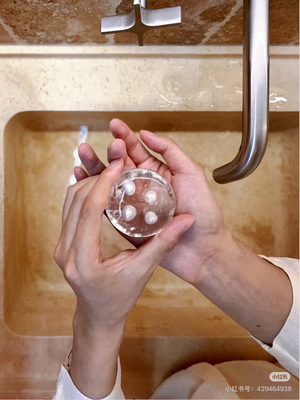 Hands holding a transparent handmade hydrating soap with four genuine freshwater pearls at a bathroom sink.